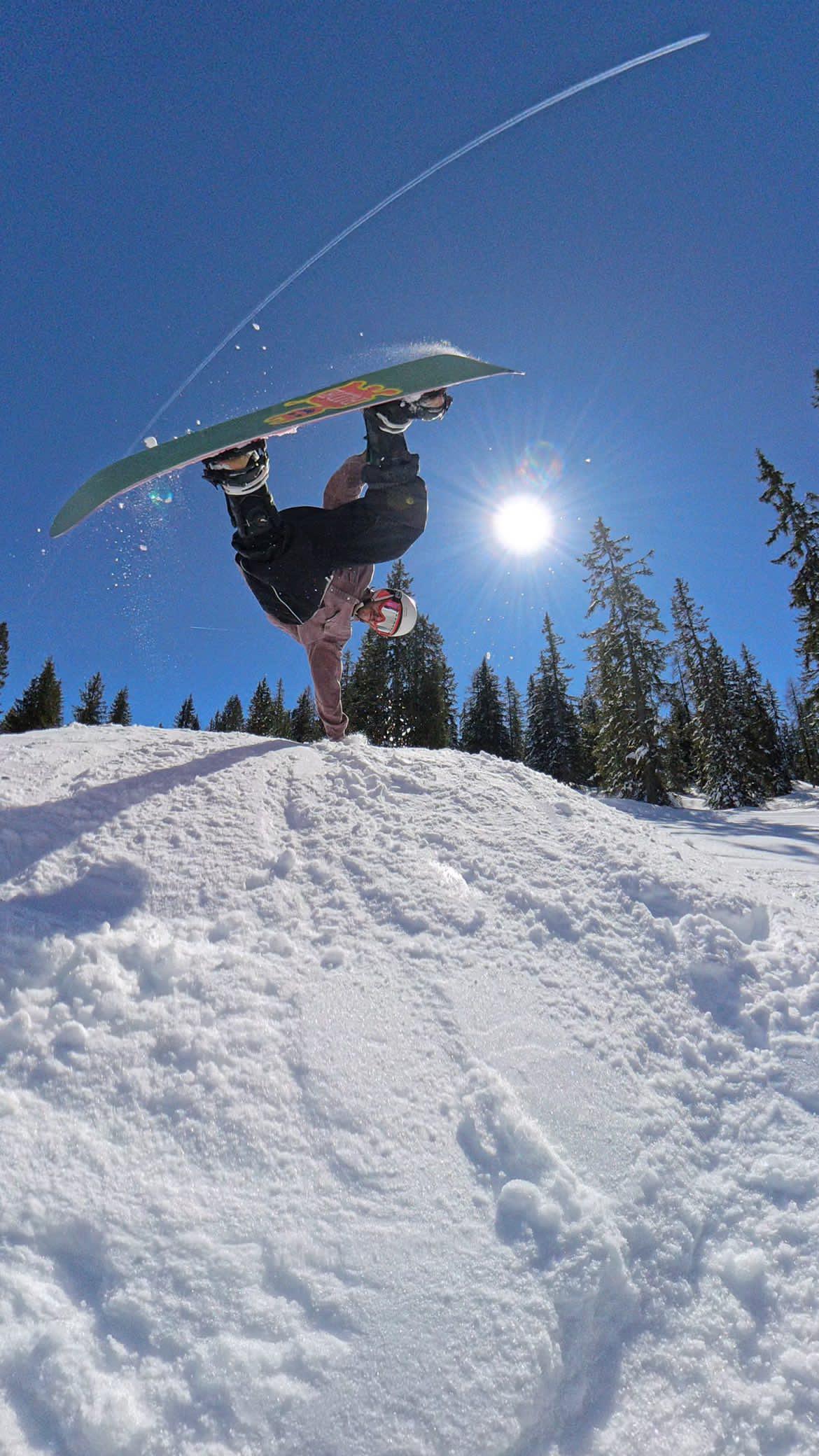 Jan throwing a handplant on his snowboard on a bluebird park day